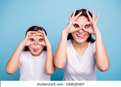 Close up photo beautiful two people brown haired mom little daughter friends look finger specs okey symbol tongue out mouth silly shapes figures wear white t-shirts isolated bright blue background