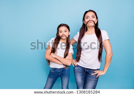 Close up photo beautiful two people brown haired mom small little daughter make moustache curls like guys man male fooling around wear white t-shirts isolated bright blue background