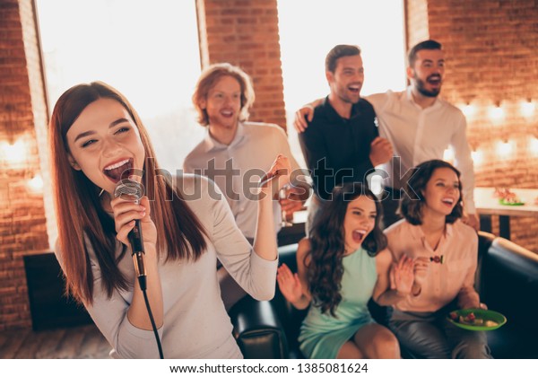 Close up photo best friends buddies karaoke\
gathering hang out sing she her ladies soloist he him his guys help\
yell shout scream words song wear dresses shirts formalwear sit\
sofa loft room indoors