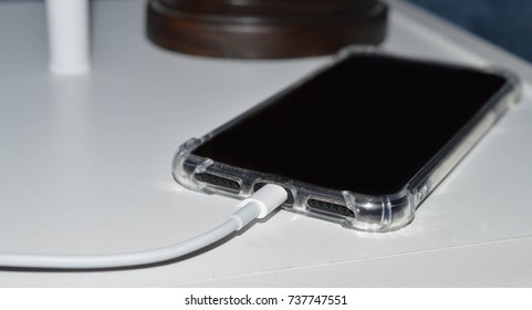 close up photo of black cell phone charging on a white bedside table 
