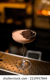 Close Up Photo Of Brown Cocktail Standing On Metal Bar Counter Decorated With Chocolate. Shelves With Bottles Of Alcohol In Background.