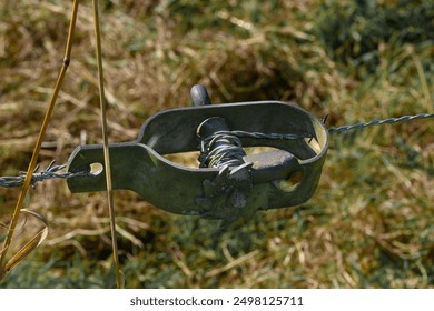 Close up photo of a cable tensioner tensioning barbed wire from a meadow, with an out of focus green grass background. - Powered by Shutterstock