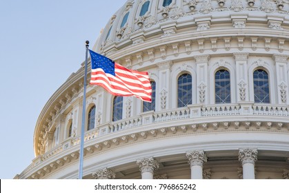 Close up photo of the Capitol Building Rotunda in Washington, D.C. with the American Flag flying proudly with a blue sky.   - Shutterstock ID 796865242