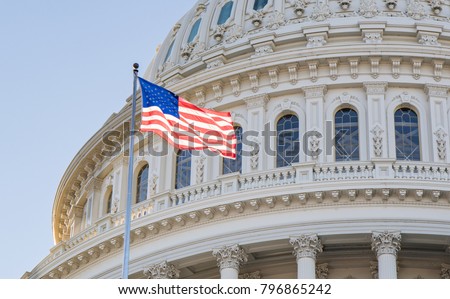Close up photo of the Capitol Building Rotunda in Washington, D.C. with the American Flag flying proudly with a blue sky.  