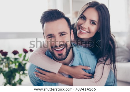 Close up photo of cheerful excited glad careless happy with toothy beaming smile brunette attractive woman and with stylish hairdo man, she is hugging him from the back
