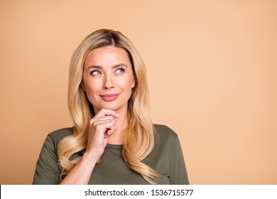 Close up photo of cheerful positive cute nice girlfriend touching her chin in green t-shirt when thinking through her doubts staring into empty space isolated beige pastel color background