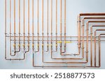 A close up photo of copper pipes, fittings, and valves in a complex plumbing system mounted on a white wall. The pipes are neatly organized and aligned, creating a geometric design.