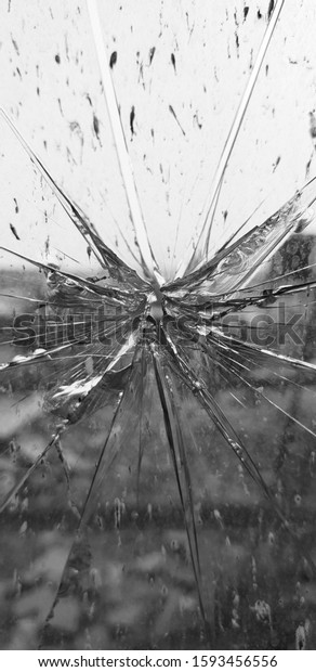 a close up photo\
of a cracked glass pane in vertical portrait orientation with a\
hole at the middle.