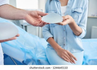 Close up photo of doctor showing silicone implant for woman during consultation in beauty clinic