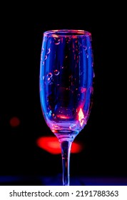 Close Up Photo Of Empty Wine Glass With Drops Of Water. Black Background And Red Light 