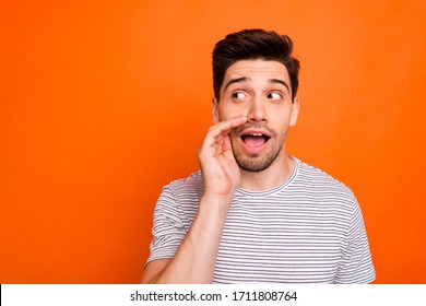 Close up photo of funky silly macho guy chatterbox hold arm near mouth telling secrets wear casual striped t-shirt isolated over bright orange color background