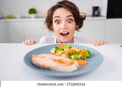 Close up photo of funny housewife lady cunning tricky hungry eyes look from under table ready to eat grilled salmon trout fillet steak garnish portion modern kitchen indoors