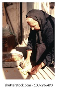 A close up photo of a grandmother while breaking almonds, dressed in traditional uniform.