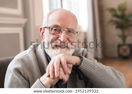 Close up photo of grey haired grandparent with walking stick head lean on hand wearing casual outfit sitting on cozy sofa. Physically disabled positive old grandfather seated on couch resting at home