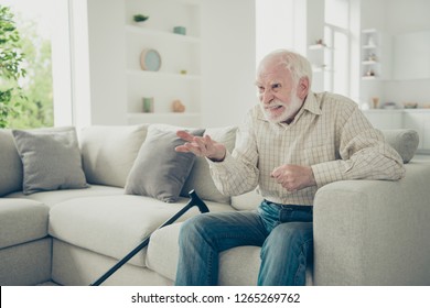Close up photo of grey haired he his him granddad with raised hand to television struggling with news presenter casual checkered shirt jeans denim outfit indoors sitting on cozy divan