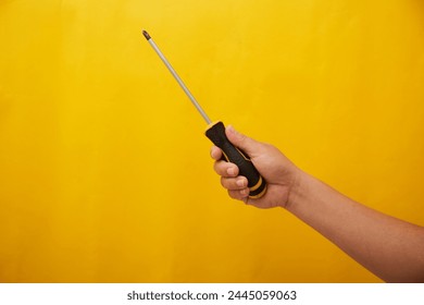 Close up photo of hand holding a screw driver on yellow background