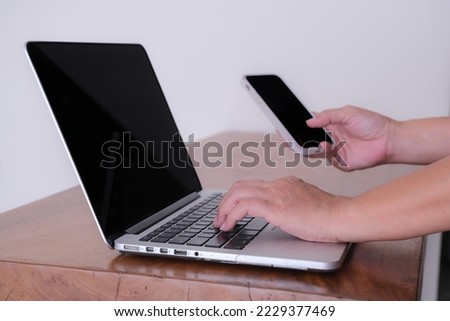 Close up photo of hands working on a laptop computer and holding a smartphone