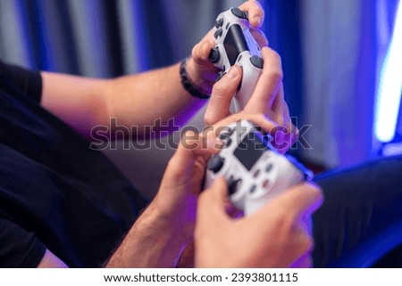Close up of photo in holding joystick, playing video game or online streamer with friends in neon blue light curtain background. Concept of sitting couch lifestyles gamer in living room. Sellable.