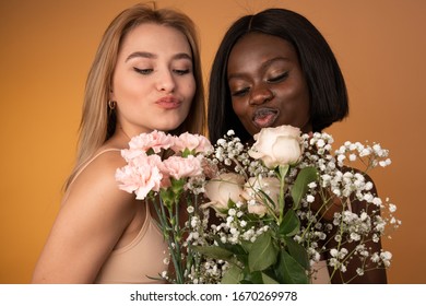 Close Up Photo Of International Girls Who Holding Spring Boquet Flowers Making Air Kiss With Closed Eyes Isolated Over Orange Background