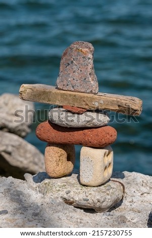 Close up photo of Inukshuk stone marker rock pile structure built from old red bricks, rocks and pieces of wood by Lake Ontario, Canada. Selective focus, blurred background and foreground.