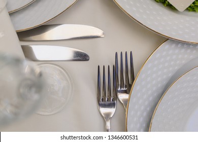 close up photo of knifes and forks near white plates and a glass on a white tablecloth