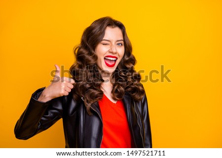 Close up photo of lady with red lips raising thumb up and winking eye wear leather jacket isolated yellow color background