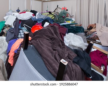 Close up photo of a large pile of household items including furniture, clothes, toilet paper, pans, pillows, toys, Christmas tree, blankets and paper almost touching the ceiling. - Shutterstock ID 1925886047