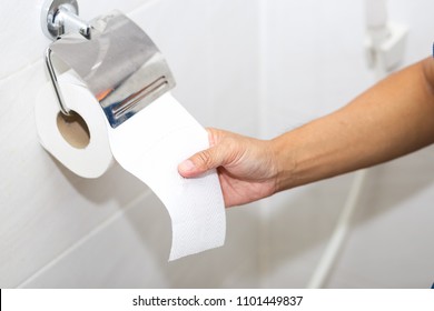 Close up photo of man sitting on toilet and using toilet paper.