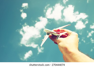 close up photo of man's hand holding toy airplane against blue sky with clouds. filtered image  - Powered by Shutterstock