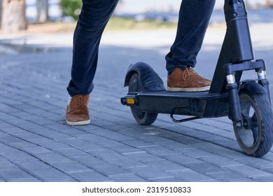 A close up photo of a modern man preparing to ride an electric scooter around town. A fashionable guy in sneakers plans a trip on a modern city transport electric scooter