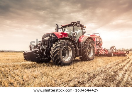 Close photo of modern red tractor with red implement seeding directly into the stubble using GPS for precision farming after a harvest with combine before the Winter. 