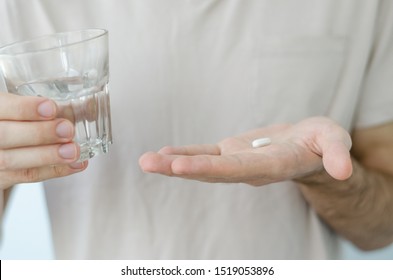Close up photo of one round pill in young male hand. Man takes medicines with glass of water. Daily norm of vitamins, effective drugs, modern pharmacy for body and mental health concept. - Shutterstock ID 1519053896
