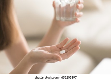 Close up photo of one round white pill in young female hand. Woman takes medicines with glass of water. Daily norm of vitamins, effective drugs, modern pharmacy for body and mental health concept