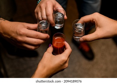 Close up photo of people,s hands toasting with mexican tequila shots and tomato juice in room