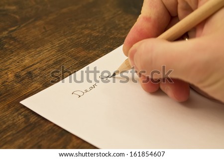 A close photo of a persons writing a letter with a pencil.