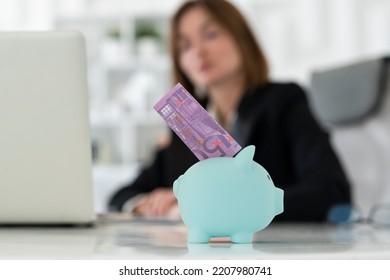 Close Up Photo Of Piggy Bank On Desktop And Stuck Banknote With Business Woman On Background In The Office	