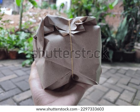 Close up photo of poor woman holding pack of rice for breakfast with herringbone 45° pattern paving blocks and plant background