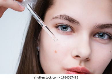 Close up photo. Portrait of a beautiful girl using a serum, applying it with a pipette on her face, getting rid of skin imperfections