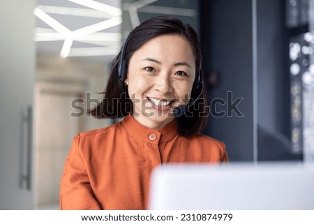 Close up photo portrait of young beautiful Asian woman, business woman smiling and looking at camera, receptionist using headset for video call, happy and successful call center worker.