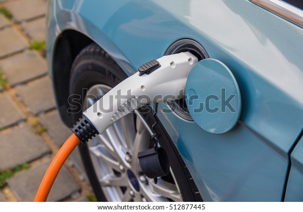 Close up photo of power plug inserted in to an\
electric vehicle on a city street. Charging the electric vehicle on\
a parking lot outdoors.
