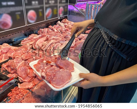 Close up photo of pregnant woman buying pork meat at supermarket