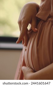 Close up photo of pregnant woman in a stylish pink peignoir touc