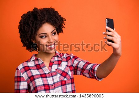 Close up photo of pretty cute lady hold hands telephone make selfies wear casual checkered plaid shirt isolated orange bright background