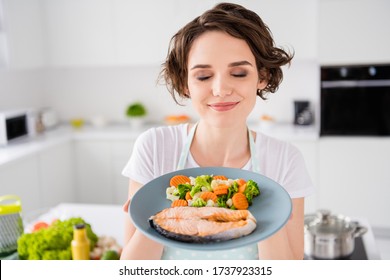 Close up photo of pretty housewife lady chef hold ready grilled salmon trout fillet steak with garnish cook dinner one person portion eyes closed wear apron t-shirt modern kitchen indoors - Powered by Shutterstock