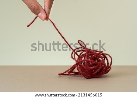 Close up photo of red loop and hand trying to untie. Concept of problem solving skills and brainstorming on confused mindset.