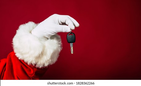 Close Up Photo Of Santa Claus Hand In White Glove Holds Key From New Apartment Or Auto Isolated On A Red Background