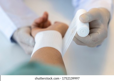 Close Up Photo With Selective Focus.Asian Orthopaedic Doctor Using The White Elastic Bandage Roll Over The Patient 's Wrist. Wrist Pain From Sport Injury. Shallow DOF.Medical Concept.