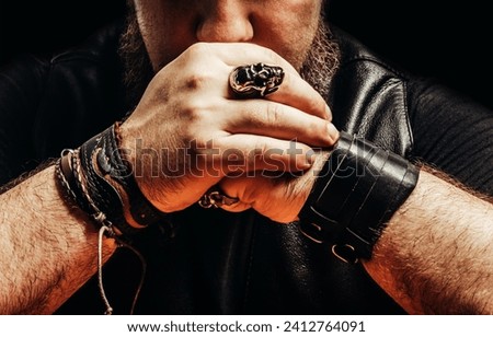 Close up photo of a shaded bearded male muscular biker with leather wrists, leather clothing, sitting by a table pose.