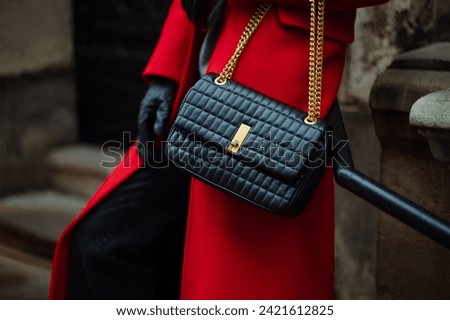 Close up photo of trendy black quilted faux leather baguette bag, purse in fashionable winter outfit. Woman wearing red coat, gloves, posing in street. Copy, empty, blank space for text
