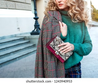 Close up photo of trendy snake bag with bored trinket in hands of fashionable woman posing in street with blooming spring trees. Wearing Fashion elements.Female fashion concept. Copy space.